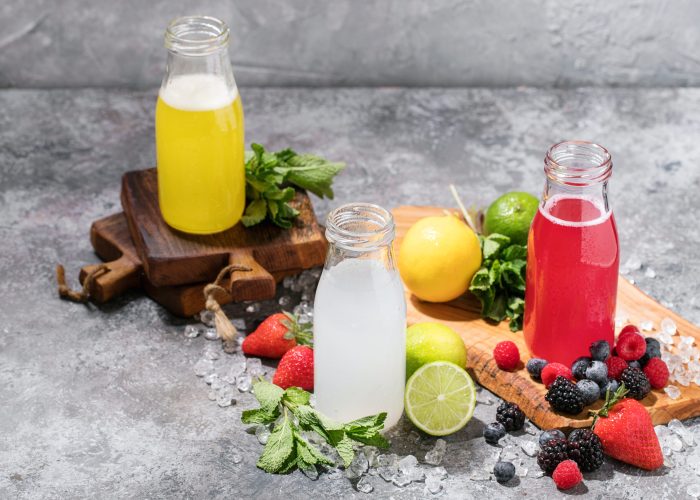 Home made raspberry and lemon lemonades served with different berries, mint, lemons and sparking water, decorated with ice.